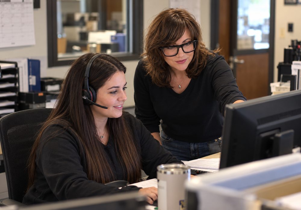 A coach working side by side with a customer service rep at her desk